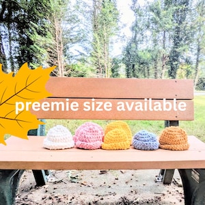 Puede incluir: Una fila de seis gorros de ganchillo pequeños y gruesos en blanco, rosa claro, amarillo brillante, amarillo mostaza, azul claro y tostado. El texto "preemie size available" está impreso en blanco sobre un gráfico de hoja de arce amarilla.