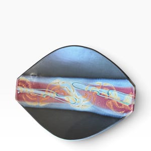 Puede incluir: Un plato de cerámica en forma de diamante con un acabado negro mate en las secciones superior e inferior. Una banda horizontal central muestra un patrón jaspeado y arremolinado de magenta intenso, azul claro y crema con un esmalte brillante.