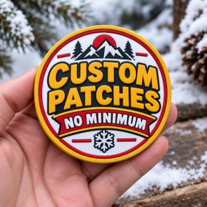 Puede incluir: Un parche circular de goma con borde amarillo, fondo blanco y detalles en rojo. El texto dice CUSTOM PATCHES en amarillo y NO MINIMUM en blanco. El diseño incluye una cordillera negra, árboles de pino y un icono de copo de nieve blanco.