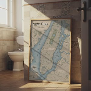 Op de afbeelding: Een ingelijste verticale kaartprint getiteld New York A City Atlas, met een gedetailleerde cartografische illustratie van Manhattan, de East River en omliggende stadsdelen, voorzien van een kompasroos en vintage typografie.