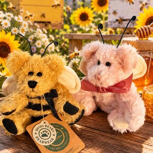 May include: Two plush teddy bears with antennae and wings. One bear is yellow with black stripes and a black bow, wearing a tag labeled Boyds Bears Archive Collection Bibi Buzzby. The other bear is light pink with a dark pink ribbon around its neck.