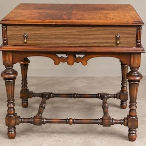 May include: A wooden side table featuring a rectangular top with a burled wood grain pattern, a single wide drawer with two brass drop pulls, and four turned legs connected by a lower stretcher base with decorative spindle detailing.