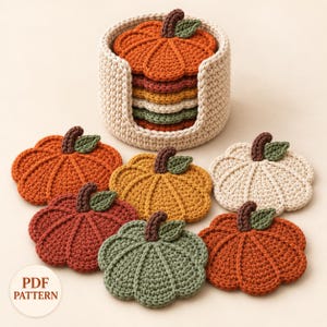 Puede incluir: Un conjunto de posavasos de ganchillo con forma de calabaza en varios colores, incluyendo naranja, amarillo, crema y verde, apilados dentro de un soporte de ganchillo color crema a juego. Se ve una etiqueta blanca con PDF PATTERN.