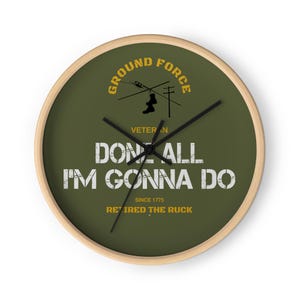Pode incluir: Um relógio de parede redondo com moldura de madeira clara e mostrador verde-oliva. O design apresenta silhuetas pretas de botas penduradas num fio, texto amarelo GROUND FORCE, VETERAN, SINCE 1775, RETIRED THE RUCK e texto branco DONE ALL I'M GONNA DO.