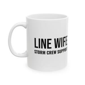 Könnte beinhalten: Ein weißer Keramikbecher mit dem schwarzen Text LINE WIFE in der oberen Zeile und STORM CREW SUPPORT in der unteren Zeile. Der Becher hat eine standardmäßige zylindrische Form mit einem geschwungenen Henkel auf der linken Seite.