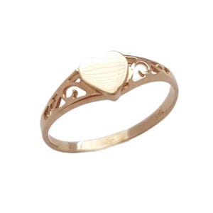 May include: A gold-toned ring featuring a smooth, solid heart-shaped centrepiece. The band is crafted with an openwork, filigree-style design on both sides, leading to a plain, polished circular shank that completes the ring's structure.