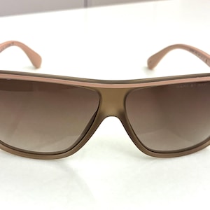 May include: Sunglasses featuring a matte brown frame with a light pink top rim accent and gradient brown lenses. The frame displays the text MARC BY MARC JACOBS on the upper corner of the right lens and includes matching light pink temples.