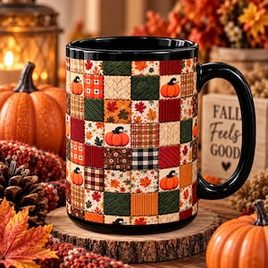 Puede incluir: Una taza de cerámica negra con un colorido patrón de parches de cuadrados con temática otoñal, que incluye calabazas naranjas, hojas de arce rojas y amarillas, cuadros marrones y texturas de punto color crema, con asa negra brillante.