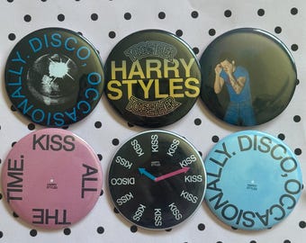 May include: A set of six circular pin-back badges featuring various designs. One badge shows a globe with the text "DISCO, OCCASIONALLY". Another displays "HARRY STYLES TOGETHER" in yellow. A third shows a person in a blue shirt. A pink badge reads "KISS ALL THE TIME". A black badge features a clock face with "KISS" and "DISCO" text. A light blue badge reads "DISCO, OCCASIONALLY".