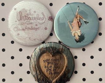 May include: Three circular pinback buttons. One is white with pink text reading The Unraveled so soon Olivia Rodrigo. One features a person on a swing against a blue sky. One has a wood-grain heart design with the text you seem pretty sad for a girl so in love.
