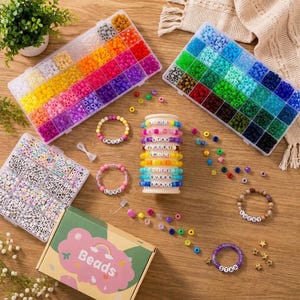 Peut inclure: Un kit de loisirs créatifs comprenant deux grands organisateurs rectangulaires en plastique remplis de perles colorées, un organisateur carré avec des perles lettres, une boîte en carton marquée "Beads" et plusieurs bracelets avec des perles lettres formant les mots LOVE, STAR, LUCKY, SMILE, NICE, QUEEN et BRAVE.
