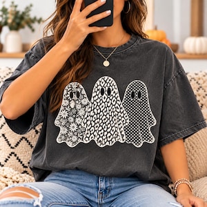 May include: A charcoal gray short-sleeve t-shirt featuring a graphic print of three ghosts. The left ghost has a white floral pattern, the center ghost has a black and white leopard print, and the right ghost has a white polka dot pattern.