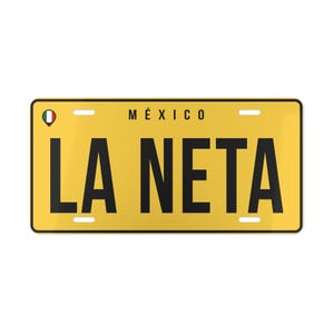 May include: A rectangular yellow license plate with a black border and black text that reads LA NETA. The word MÉXICO is printed in black above the main text. A small circular icon featuring the green, white, and red colors of the Mexican flag is located in the upper left corner. The plate includes four mounting slots.