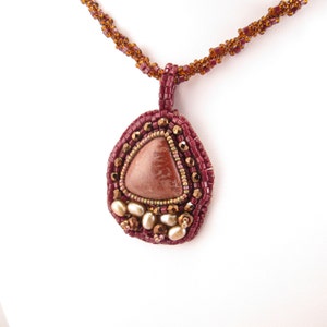 May include: A maroon beaded necklace with a pendant featuring a triangular stone surrounded by smaller beads in shades of maroon, gold, and white.