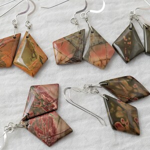 May include: A set of six diamond-shaped earrings made from polished, multi-colored stone. The earrings are attached to silver hooks.