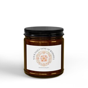 May include: A brown glass candle jar with a black screw-top lid. The white label features a circular illustration of seashells and flowers with the text "YOUR DAILY DOSE OF WHIMSEA" and "MARIHADAbyJEA" printed in a dark grey serif font.