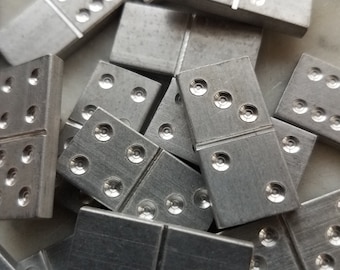 Puede incluir: Primer plano de una pila de fichas de dominó de metal plateado. Las fichas de dominó están dispuestas en un patrón aleatorio, con algunas de ellas superpuestas.
