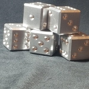 Puede incluir: Cinco dados de metal plateado con bordes redondeados y puntos en relieve en cada cara. Los dados están apilados uno encima del otro.
