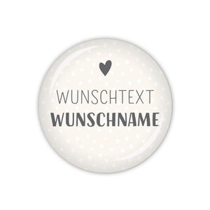 Könnte beinhalten: Weißer runder Knopf mit einem grauen Herzen und weißen Punkten. Der Text "WUNSCHTEXT WUNSCHNAME" ist in Grau gedruckt.