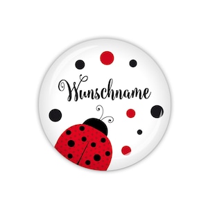 Könnte beinhalten: Ein weißer runder Knopf mit einem roten Marienkäfer mit schwarzen Punkten, schwarzen Punkten und roten Punkten drumherum. Der Text "Wunschname" ist in schwarzer Kursivschrift auf dem Knopf geschrieben.
