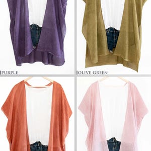 May include: Four open-front cover-ups in purple, olive green, rust orange, and pink. Each is paired with a white top and denim shorts. The cover-ups are hanging on wooden hangers against a white background. The colors are labeled below each cover-up.