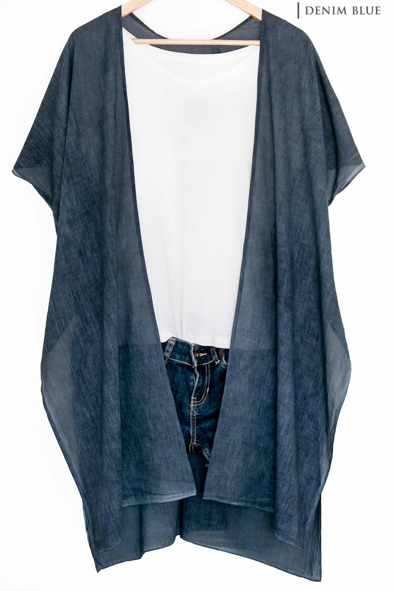 May include: A denim blue kimono-style cover-up with short sleeves, layered over a white t-shirt and blue jeans. The cover-up has a flowing, open design. The text "| DENIM BLUE" is in the upper right corner.