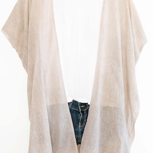 May include: Beige open-front kimono-style cover-up over a white top and denim shorts. The cover-up is made of a lightweight fabric and hangs on a wooden hanger. The word "FAVORITE" is in a box in the upper right corner.