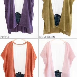 May include: Four open-front cover-ups in purple, olive green, rust orange, and pink. Each is paired with a white top and denim shorts. The cover-ups are hanging on wooden hangers against a white background.