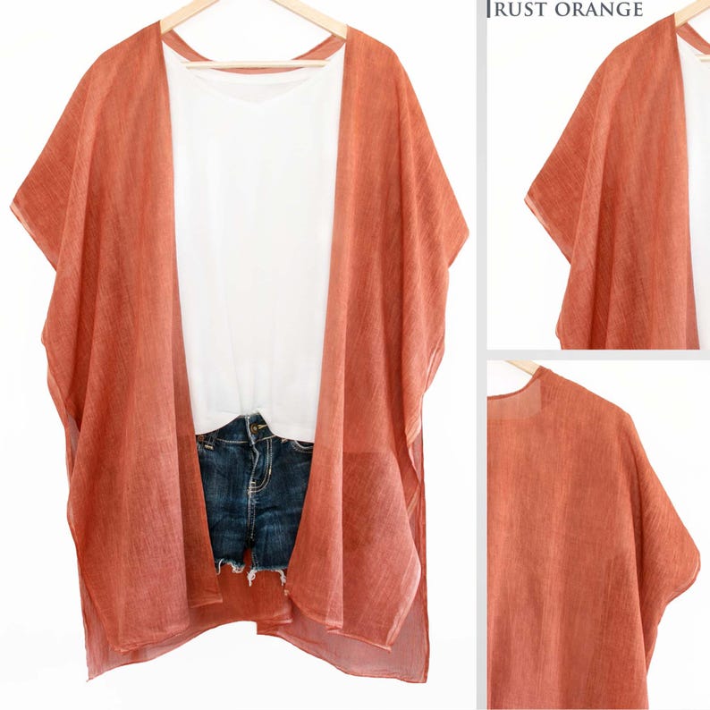 May include: Rust orange kimono-style cover-up over a white t-shirt and denim shorts. The cover-up is lightweight and flowing, with wide sleeves. The outfit is displayed on a wooden hanger against a white background.