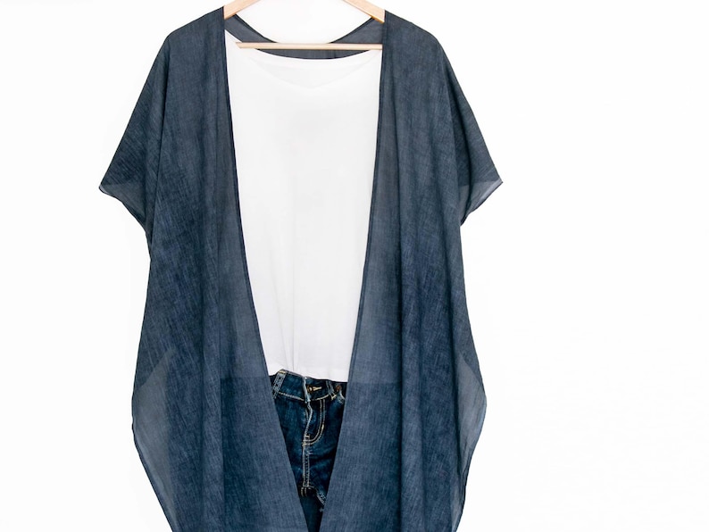 May include: A navy blue open-front kimono-style top with short sleeves, hanging on a wooden hanger. A white t-shirt and blue jeans are visible underneath the kimono. The kimono has a sheer, lightweight appearance.