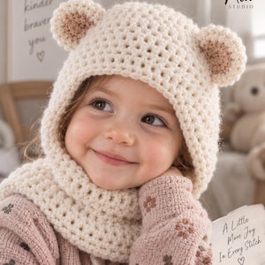 Puede incluir: Un gorro de ganchillo de color crema con dos orejas de oso redondeadas en la parte superior. El gorro tiene una construcción de hilo grueso y texturizado que cubre la zona de la cabeza y el cuello. Una etiqueta blanca muestra el texto A Little More Joy In Every Stitch.