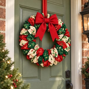 May include: A circular fabric wreath featuring a mix of red, dark green, and cream-colored cloth segments with festive patterns of holly leaves, berries, and gold stars. A large, solid red fabric bow is attached to the top center of the wreath.