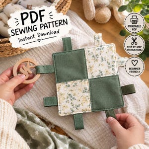 Puede incluir: Un juguete sensorial cuadrado de tela con un diseño de patchwork de cuadrados verde oliva sólidos y estampados florales, con múltiples pestañas de tela en los bordes y un anillo de madera redondo, presentado como patrón de costura PDF descargable.
