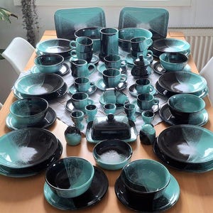 Puede incluir: Un gran juego de vajilla de cerámica con un diseño bicolor, que presenta una base negra profunda y un esmalte turquesa vibrante que se desvanece hacia un centro blanco moteado. Incluye platos, cuencos, tazas, hueveras y una mantequera.