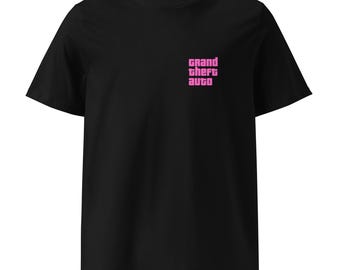May include: A black short-sleeved t-shirt featuring the text Grand Theft Auto printed in a bold pink font on the upper left chest area. The garment has a crew neckline and a standard fit, showcasing a clean design on a solid black fabric base.