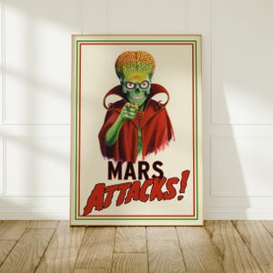 Puede incluir: Un póster rectangular que muestra a un marciano verde con un cerebro grande y expuesto, vistiendo una capa roja y señalando hacia adelante. El texto MARS ATTACKS! está impreso en letras rojas negritas en la parte inferior, dentro de un borde fino.