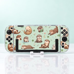 May include: A handheld gaming console featuring a light green skin decorated with a repeating pattern of brown otters in various poses, including swimming, sleeping, and playing, interspersed with small white flowers, green leaves, and bubbles.