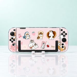 Può includere: Una custodia protettiva rosa chiaro per console di gioco portatile con varie illustrazioni di gatti, tra cui un gatto in costume da squalo, un gatto dentro una fetta di pane, un gatto su un pancake e un gatto seduto accanto a una fetta di torta.