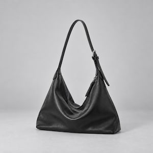 May include: A black hobo-style shoulder bag with a smooth, matte finish. The bag features a single adjustable strap with a silver-toned metal buckle, a slouchy triangular silhouette, and a zipper closure with a matching black leather pull tab.