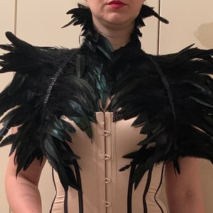 Könnte beinhalten: Ein schwarzer Federkragen und ein Schulterstück mit einem schwarz-weißen Korsett darunter.