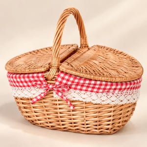 May include: An oval-shaped woven wicker basket featuring a hinged double-lid design and a central handle. The interior is lined with a red and white gingham fabric, accented by a white lace trim and a small fabric bow on the front.