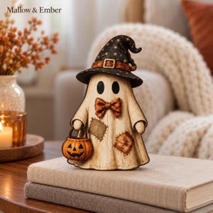 Pode incluir: Uma figura de fantasma Mallow & Ember usando um chapéu de bruxa preto com estrelas douradas e fivela castanha, uma gravata borboleta xadrez e dois remendos no corpo creme. O fantasma segura um pequeno balde de abóbora laranja.
