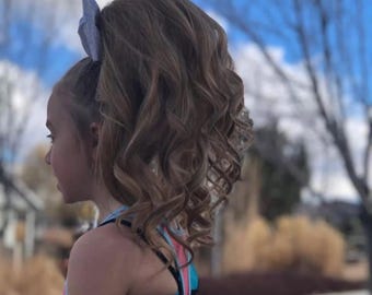 Peut inclure: Un nœud pour cheveux gris clair à paillettes fixé sur une queue-de-cheval haute avec des boucles volumineuses en cascade. Les cheveux sont coiffés en hauteur, mettant en valeur les mèches ondulées et la surface scintillante du nœud.