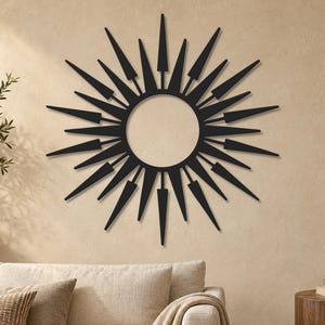 May include: A black metal wall art piece featuring a circular center surrounded by radiating spikes of varying lengths and widths, creating a sunburst pattern. The design consists of alternating long, pointed rays and shorter, wider rays.