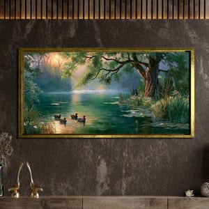 May include: A rectangular landscape painting in a gold frame depicting a serene river scene with three ducks swimming in calm green water. A large tree with overhanging branches stands on the bank, illuminated by soft sunlight filtering through.