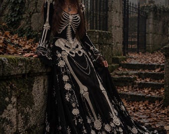 May include: A floor-length black gown featuring a white skeletal rib cage and pelvic bone print on the bodice. The long-sleeved dress includes intricate white floral embroidery, lace detailing, and a spiderweb pattern along the hemline.