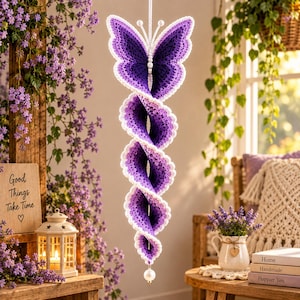 May include: A hanging spiral decoration crafted from purple and white yarn, featuring a butterfly-shaped top with white pearl accents. The crochet structure transitions from a deep violet center to lighter lavender edges, ending in a single white pearl.