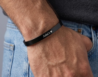 May include: A matte black cuff bracelet featuring a smooth, minimalist band design. The surface of the bracelet is engraved with the white text "Asha's" followed by a small heart symbol, creating a clean and simple aesthetic for the wrist.