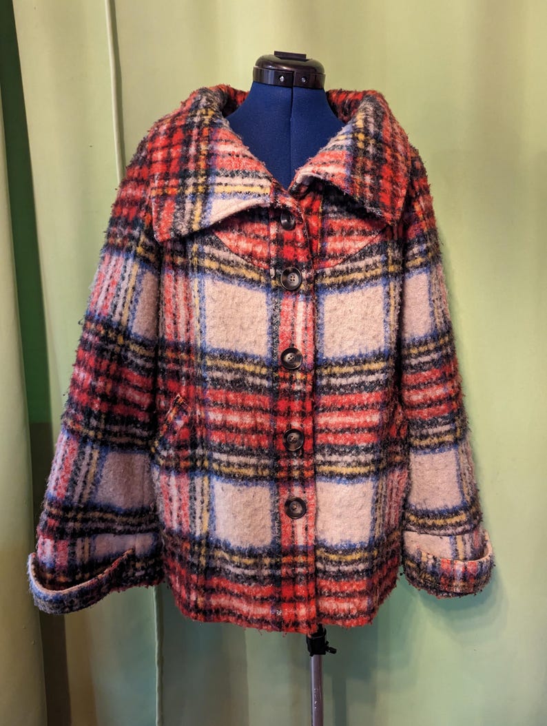 May include: A plaid jacket in red, black, yellow, and beige. The jacket has a wide collar, button closure, and two front pockets. The sleeves are cuffed. The jacket is displayed on a blue dress form.