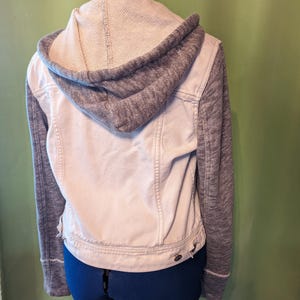 Op de afbeelding: Een lichtbeige spijkerjasje met een grijze gebreide capuchon en mouwen. De jas heeft een knoopsluiting en een klassiek ontwerp, perfect voor casual wear. De achterkant van de jas is zichtbaar en toont de stikseldetails.